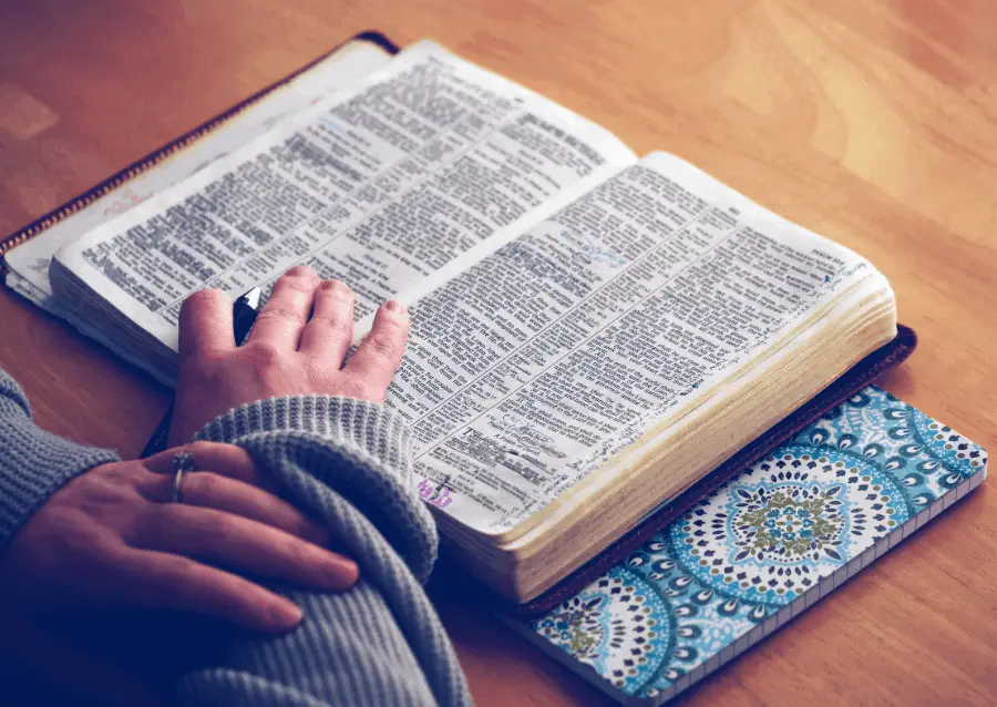 Person Reading Bible On Wooden Table With Hand On It