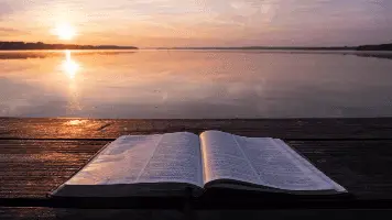 Bible On Table Near Water And Sun