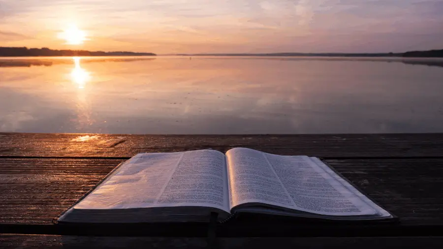 Bible On Table Near Water And Sun 900x506